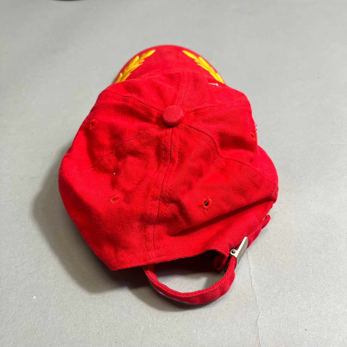Red cap with yellow embroidery on a gray surface, viewed from the back.