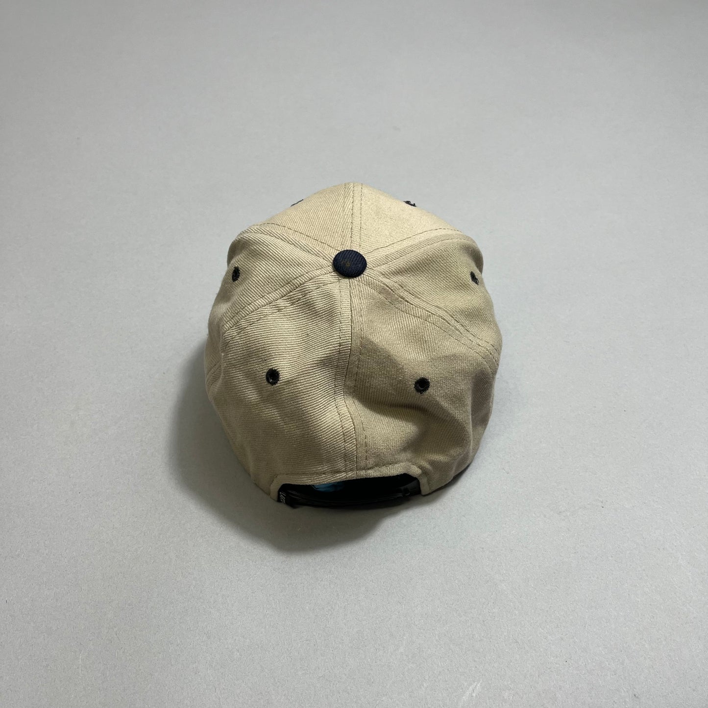 A beige cap with black eyelets and top button, viewed from the back.