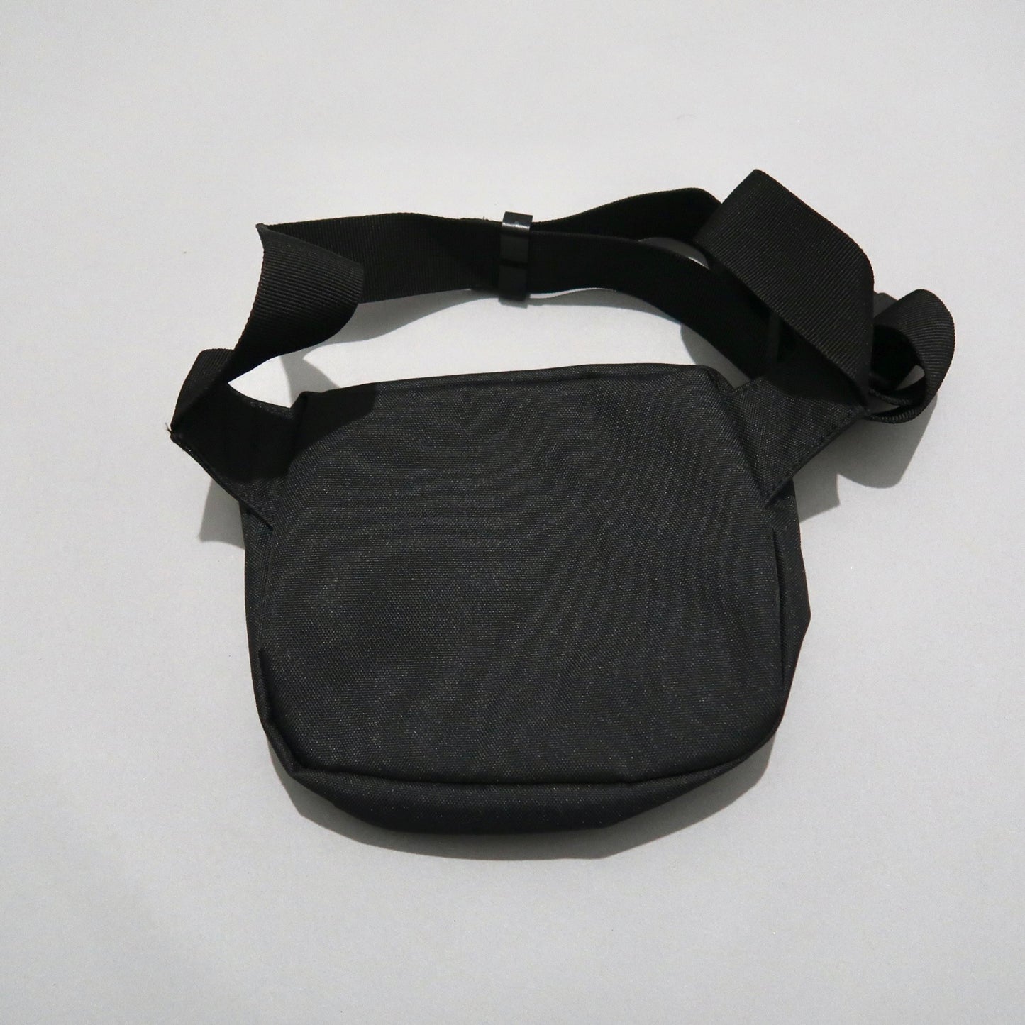 Black crossbody bag with adjustable strap on a gray background.