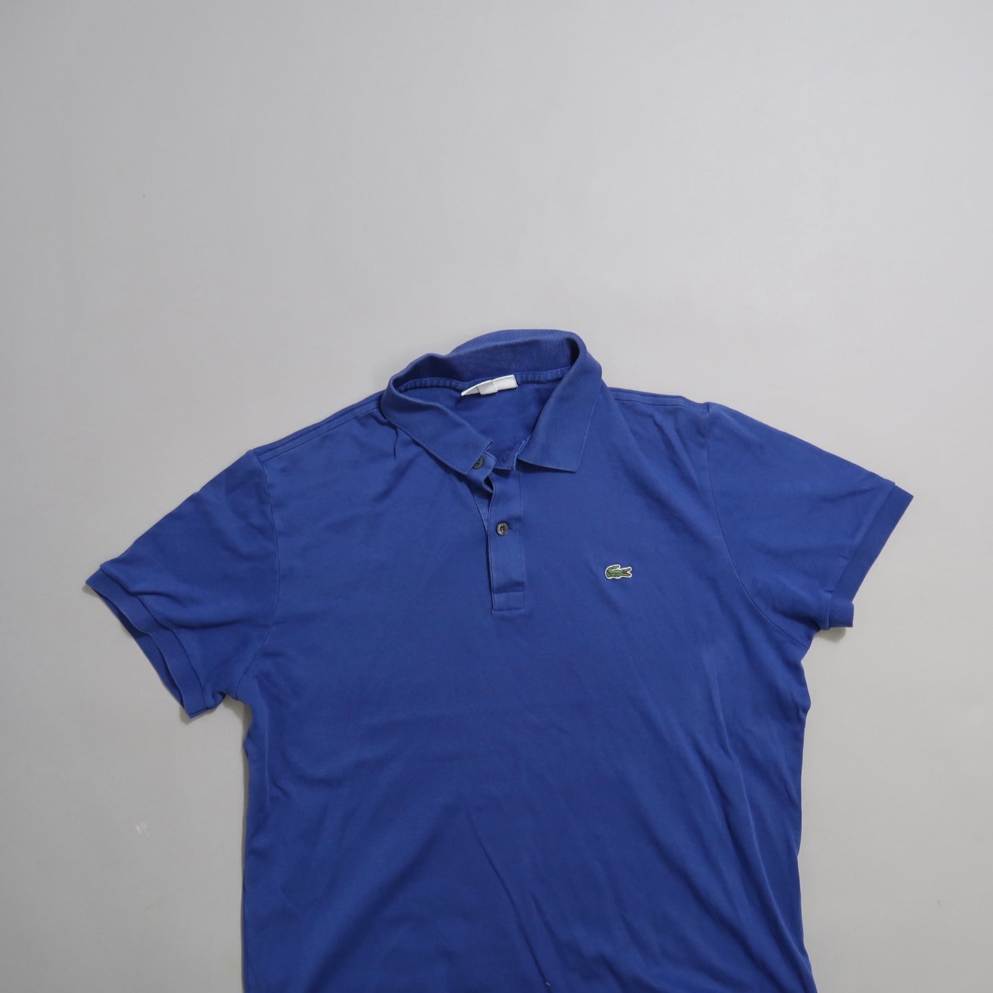 Blue polo shirt with a green logo on a plain gray background.