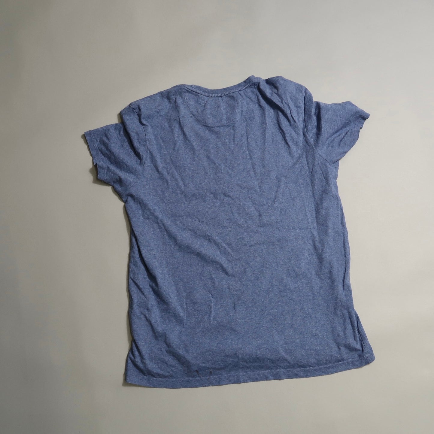 Wrinkled blue t-shirt laid flat on a gray background.