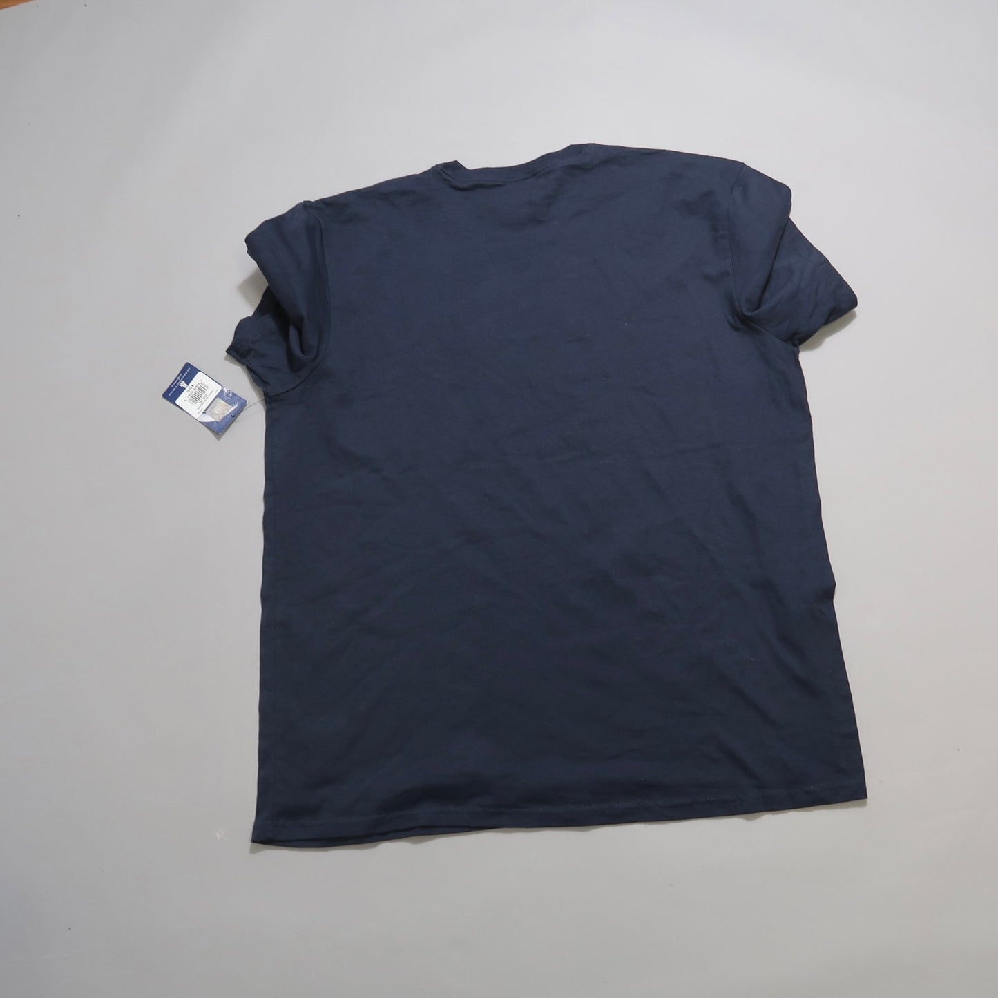 Navy blue T-shirt with a tag, lying flat on a white surface.