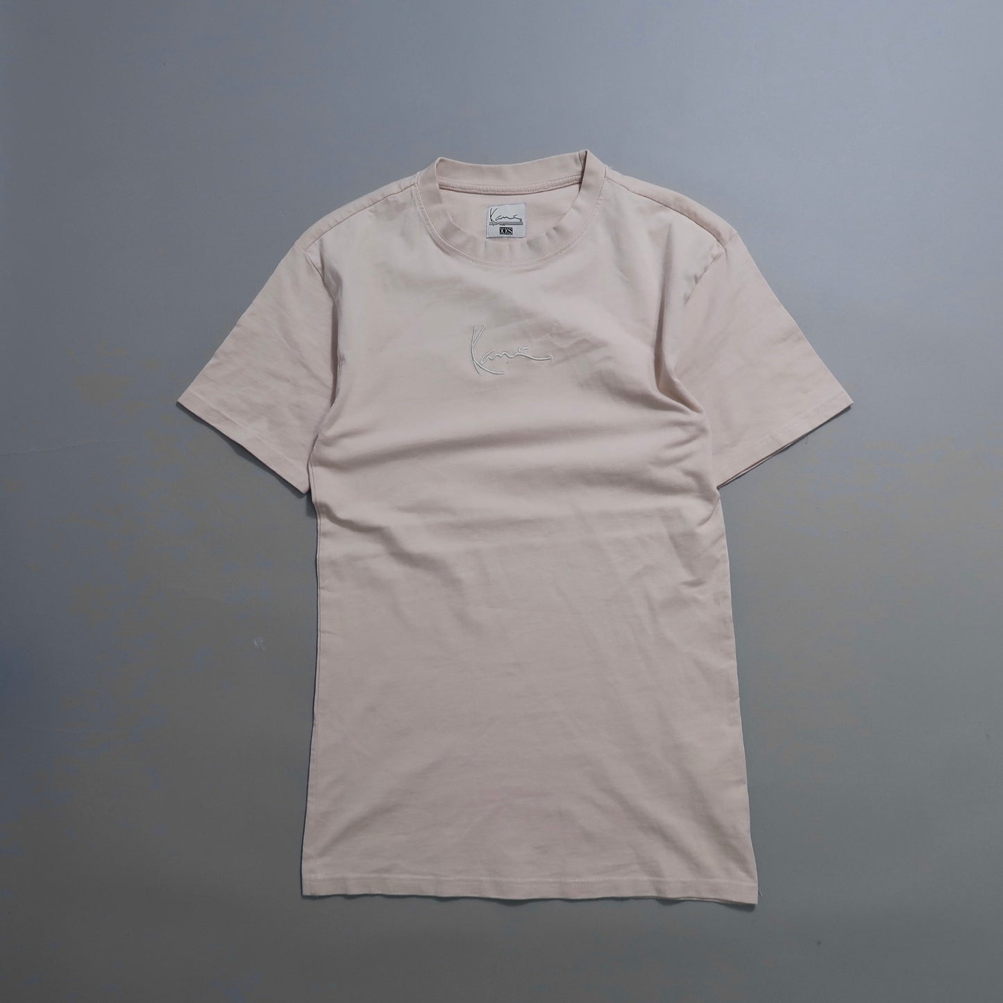 Plain beige t-shirt with embroidered design on a gray background.