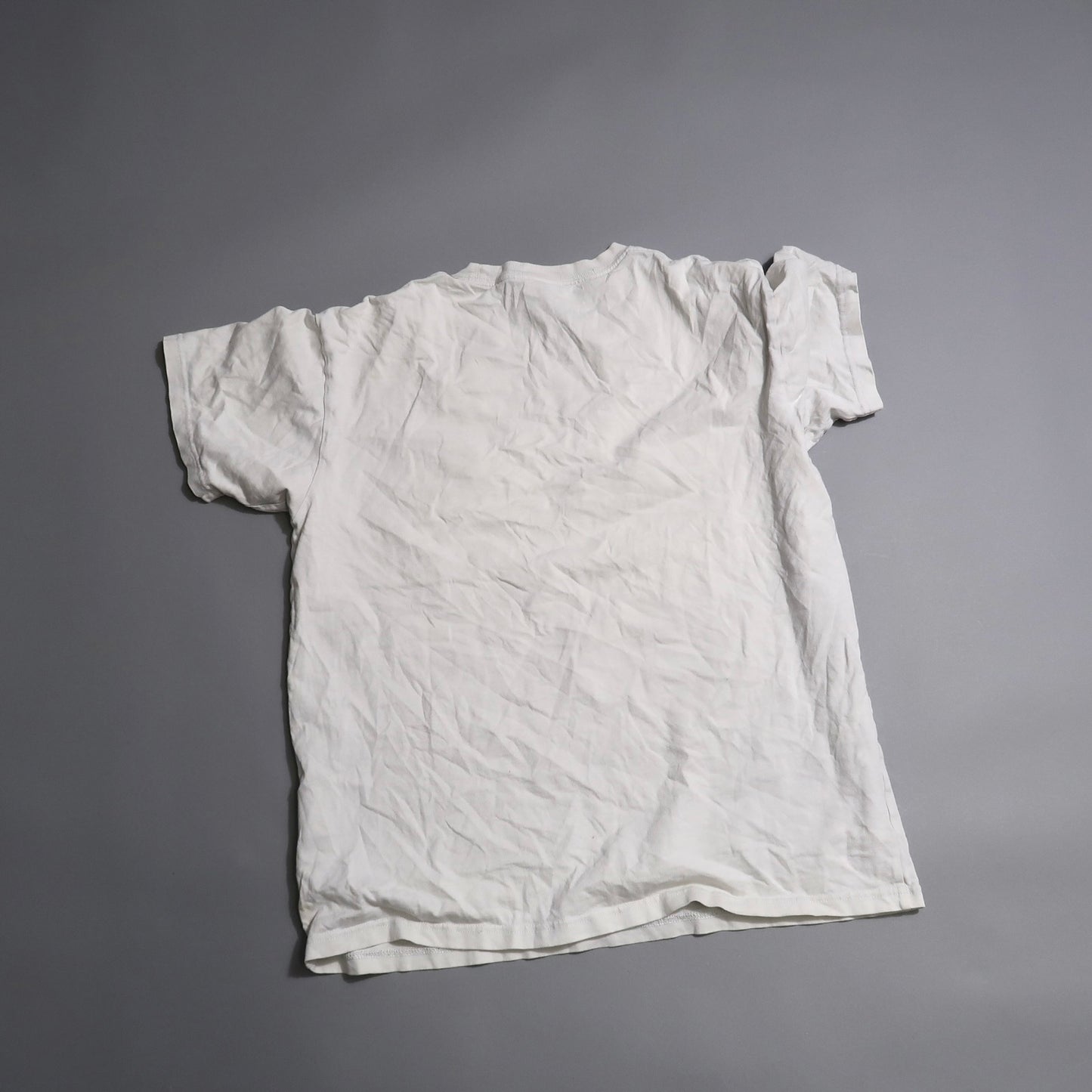 Crumpled white T-shirt laid flat on a gray surface.
