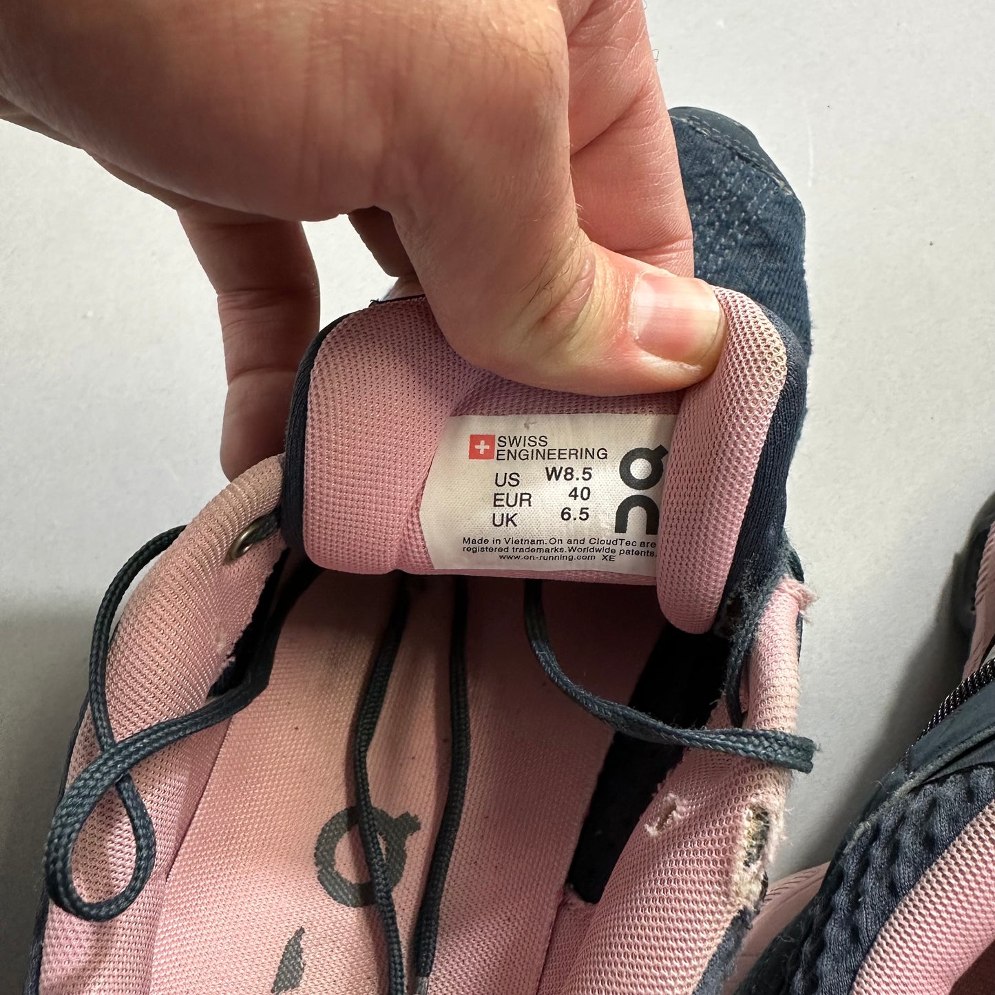 Hand holding pink shoe tongue showing size label, Swiss engineering.