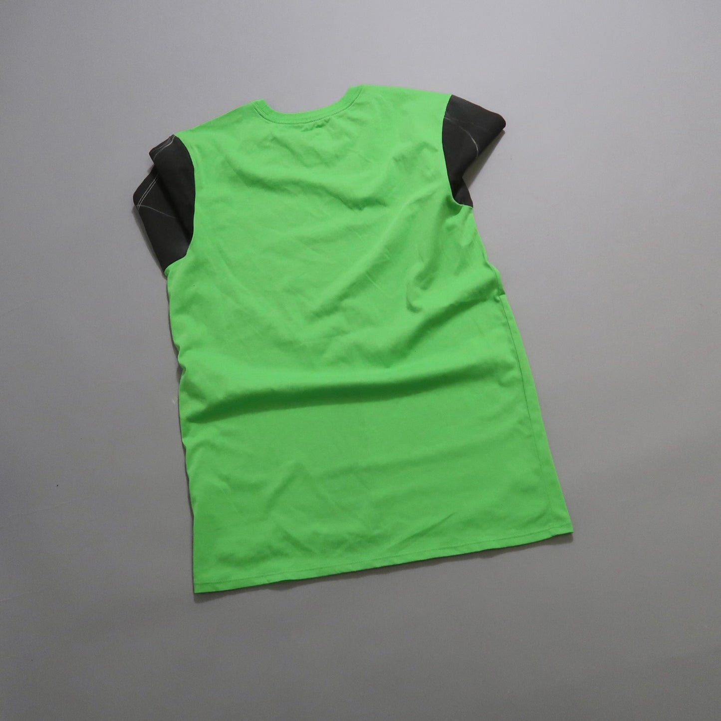 Green shirt with black shoulder accents lying flat on a gray surface.