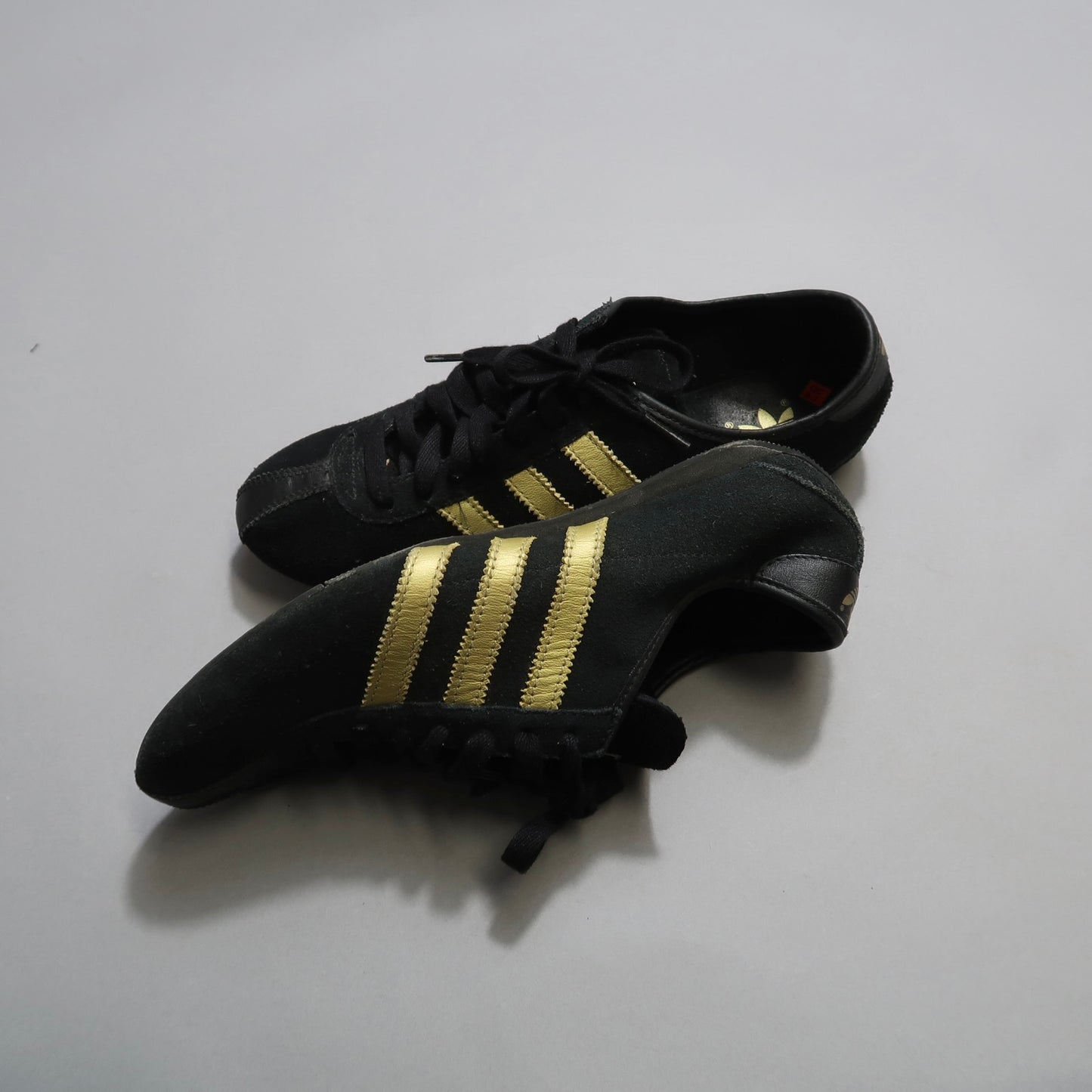 Black athletic shoes with gold stripes on a light background.