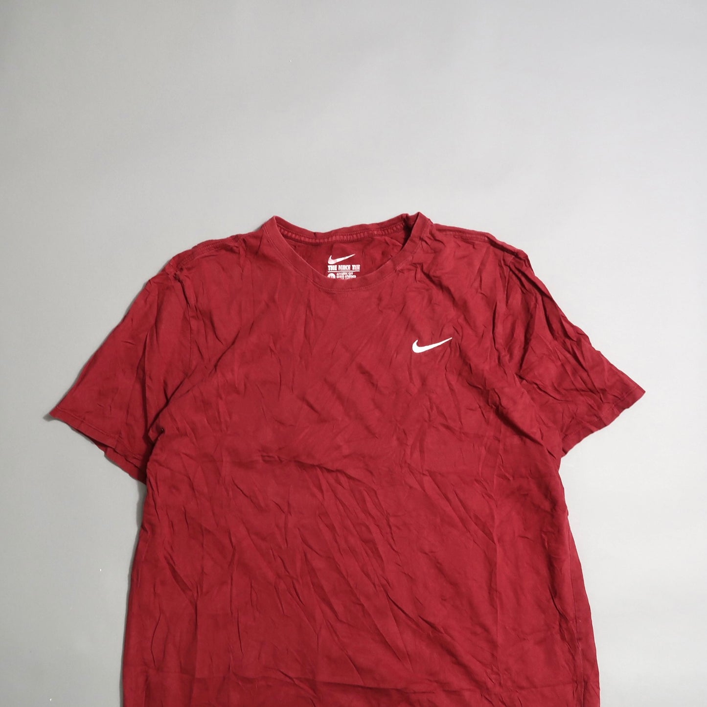 Red T-shirt with a white swoosh logo on a gray background.