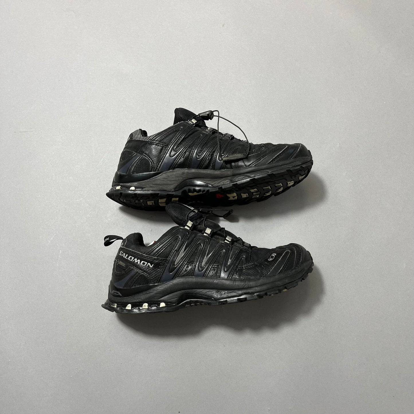 Black trail running shoes on a plain gray background.