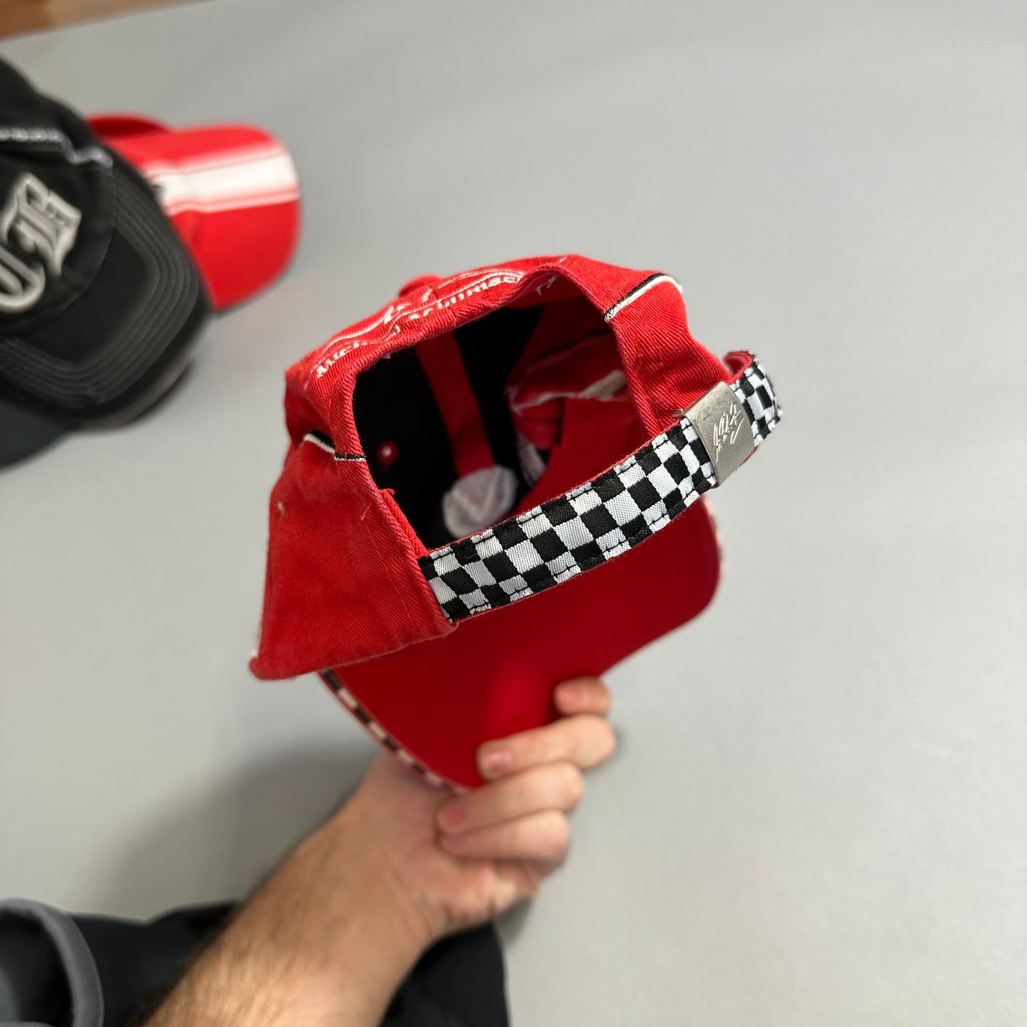 Red cap with checkered strap held in hand, gray background.