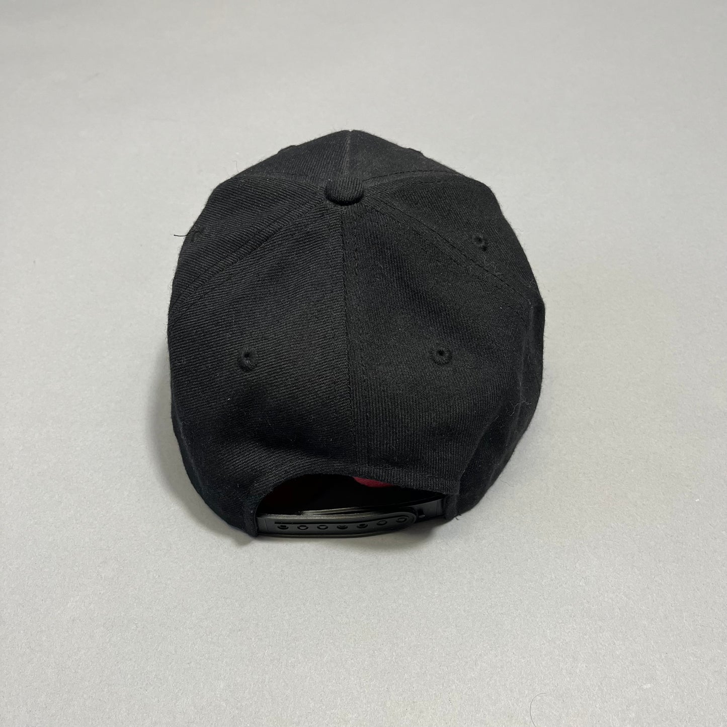 Black snapback cap on a neutral background, viewed from behind.