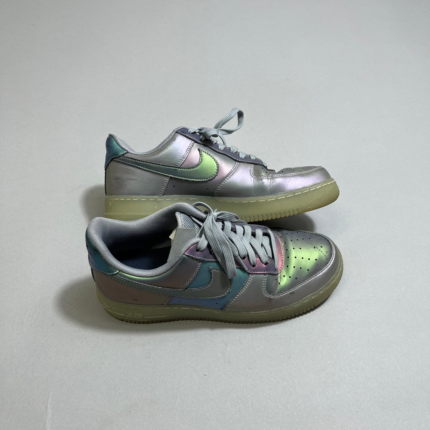 Iridescent sneakers with gray laces and gum soles on a gray surface.
