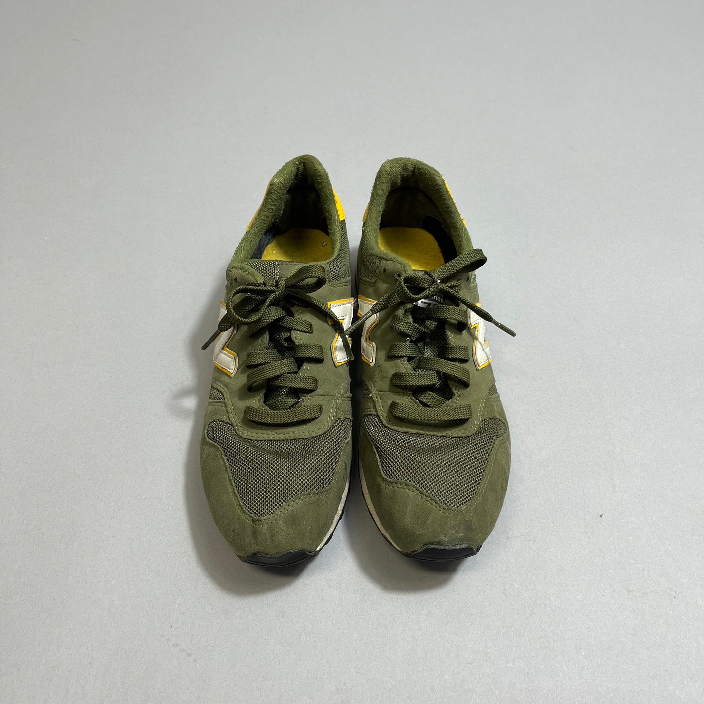 Green sneakers with black laces on a gray surface.