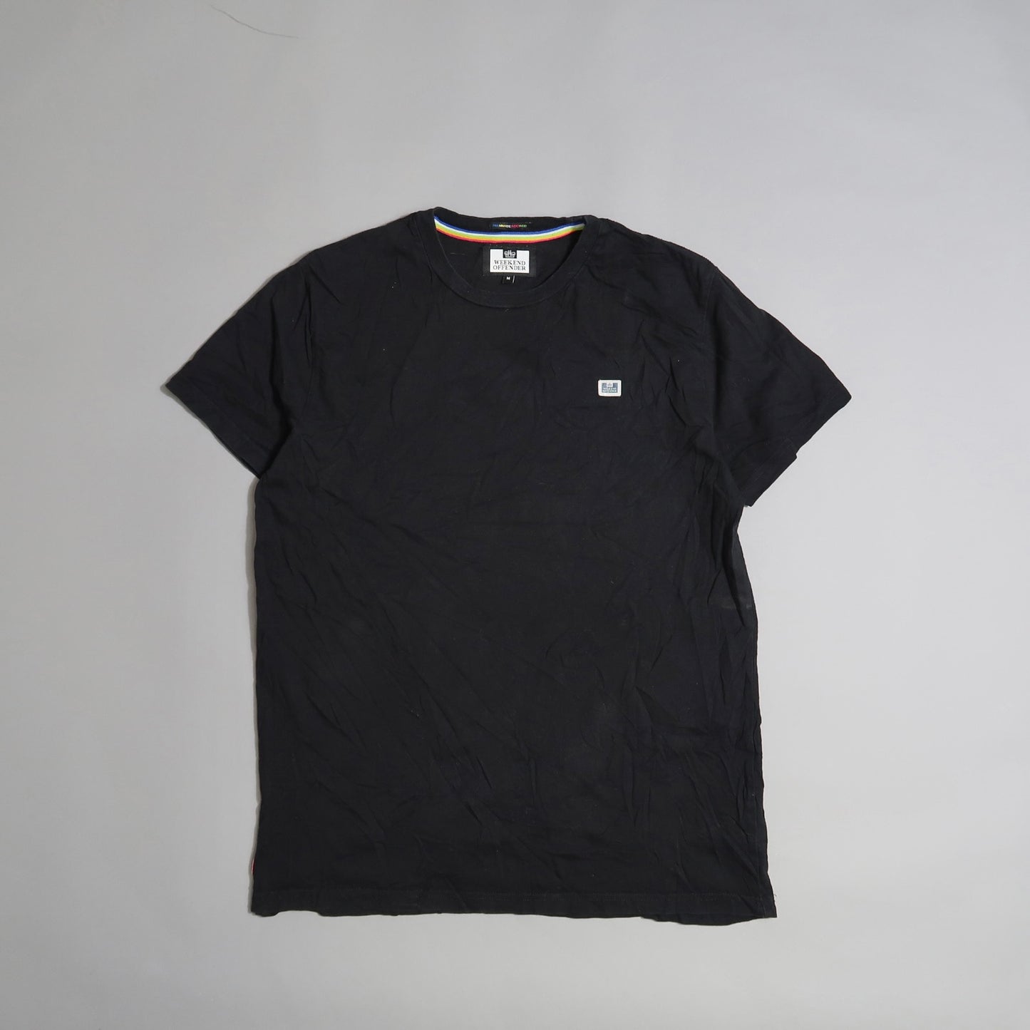 Black T-shirt with a small square logo on a plain background.