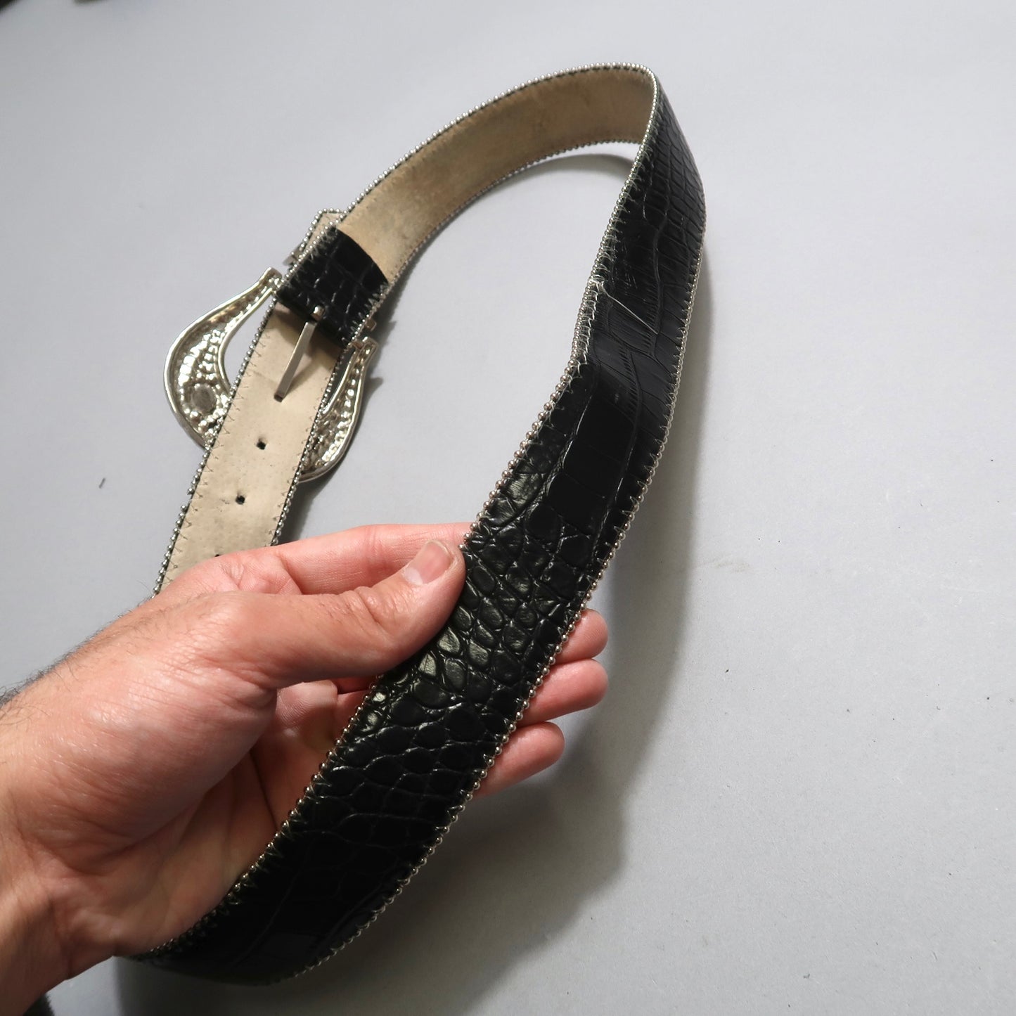 Hand holding a black textured belt with ornate silver buckle.