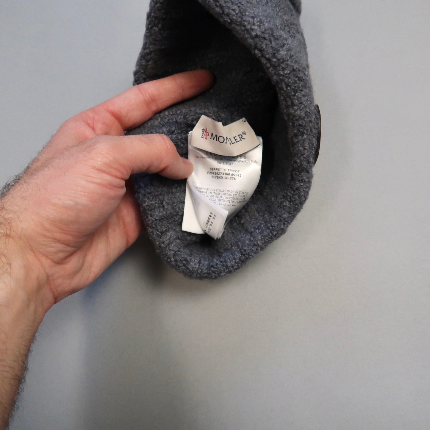 Hand holding a gray hat, label showing inside.