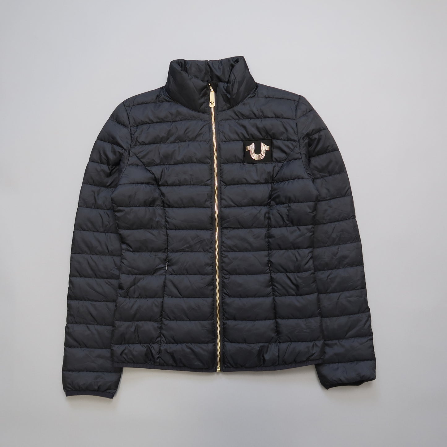 Black quilted jacket with a gold zipper and logo on the chest.