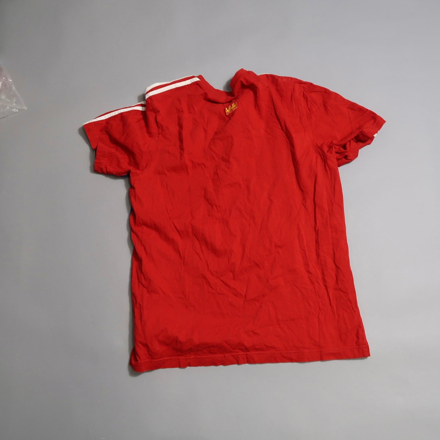 Wrinkled red t-shirt with white stripes on the shoulder, back view.