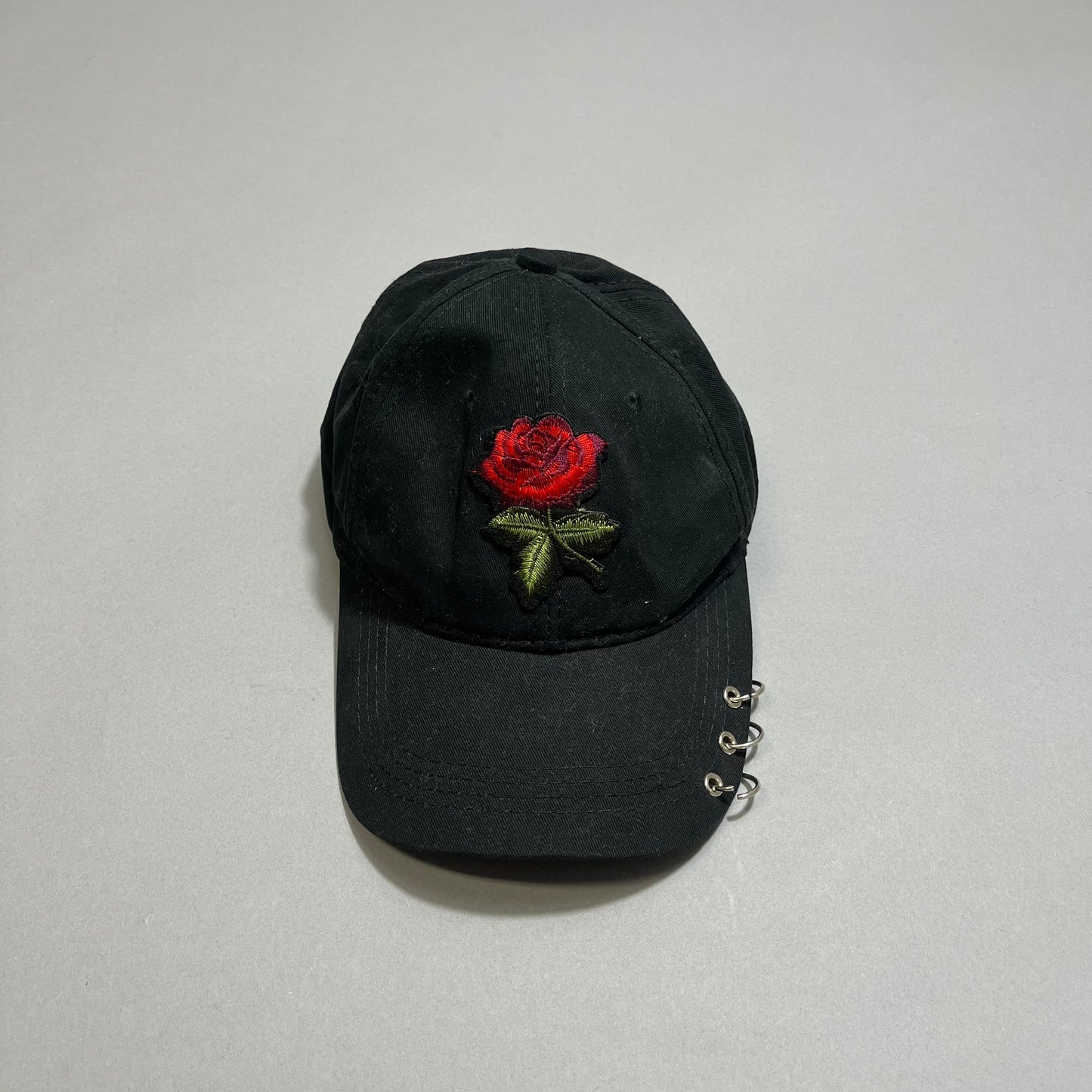 Black cap with red rose embroidery and metal rings on the brim.