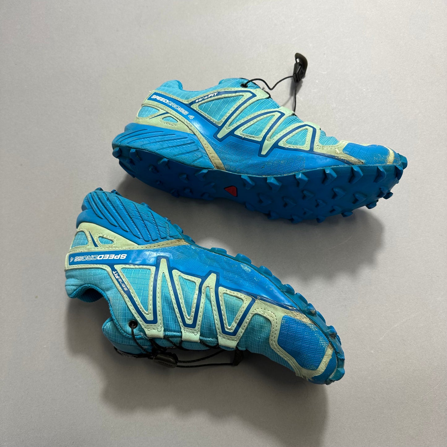 Blue trail running shoes with rugged soles on a gray background.