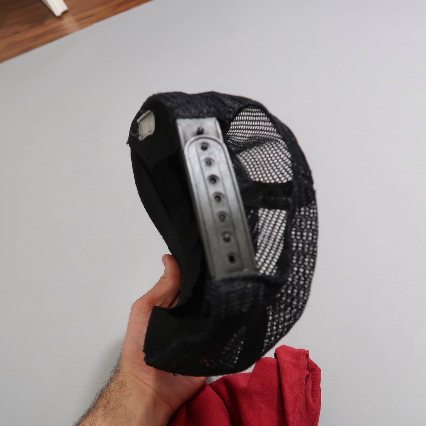Hand holding an upside-down black mesh cap with adjustable strap.