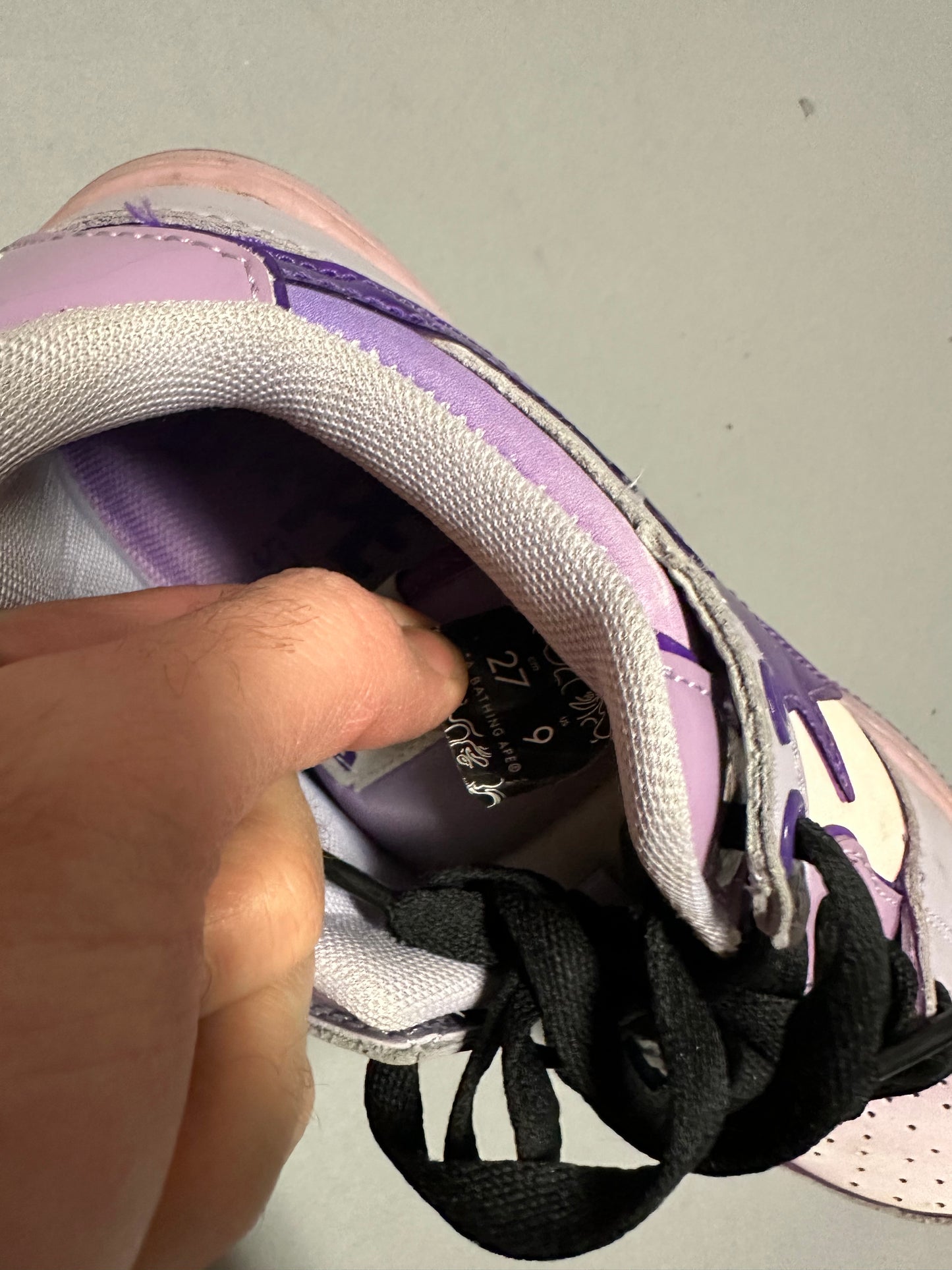 Hand holding open a purple sneaker, revealing size tag inside.