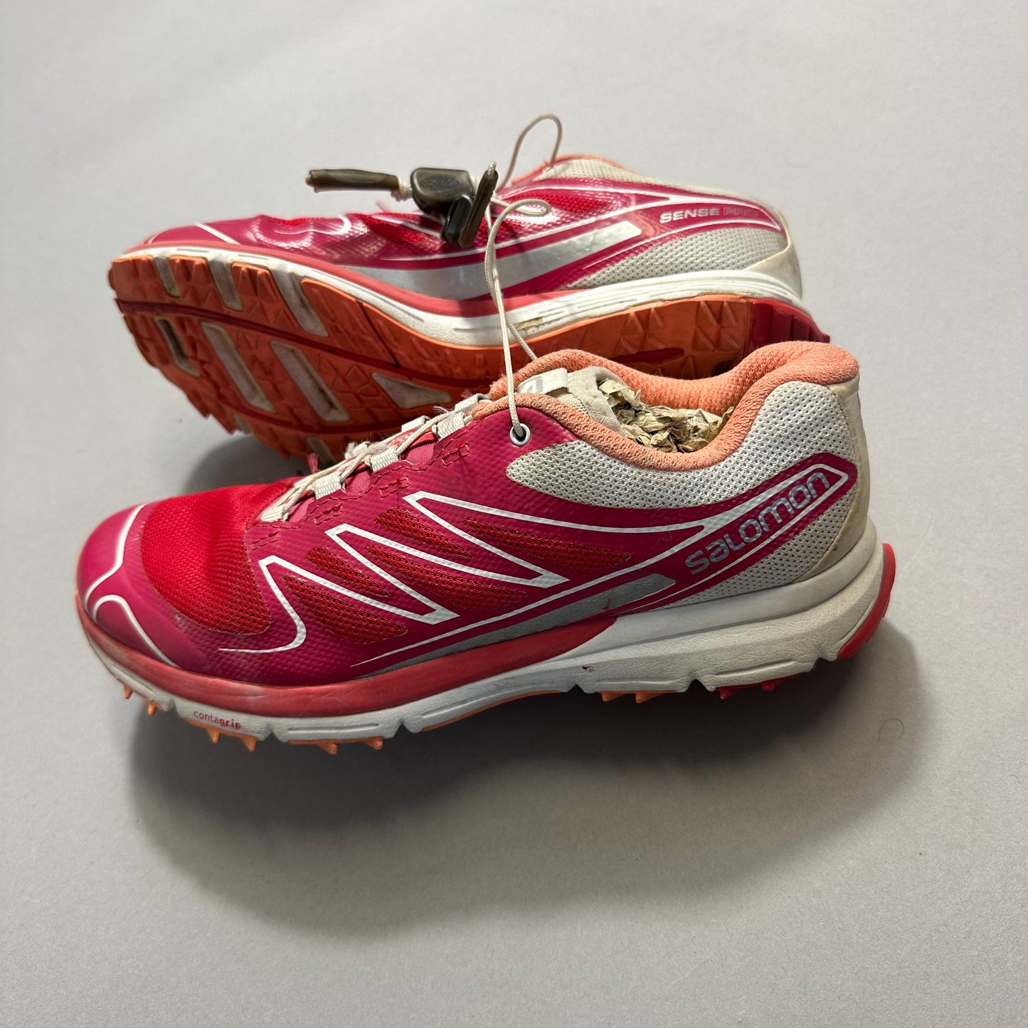 Red and white trail running shoes with lace locks on gray background.