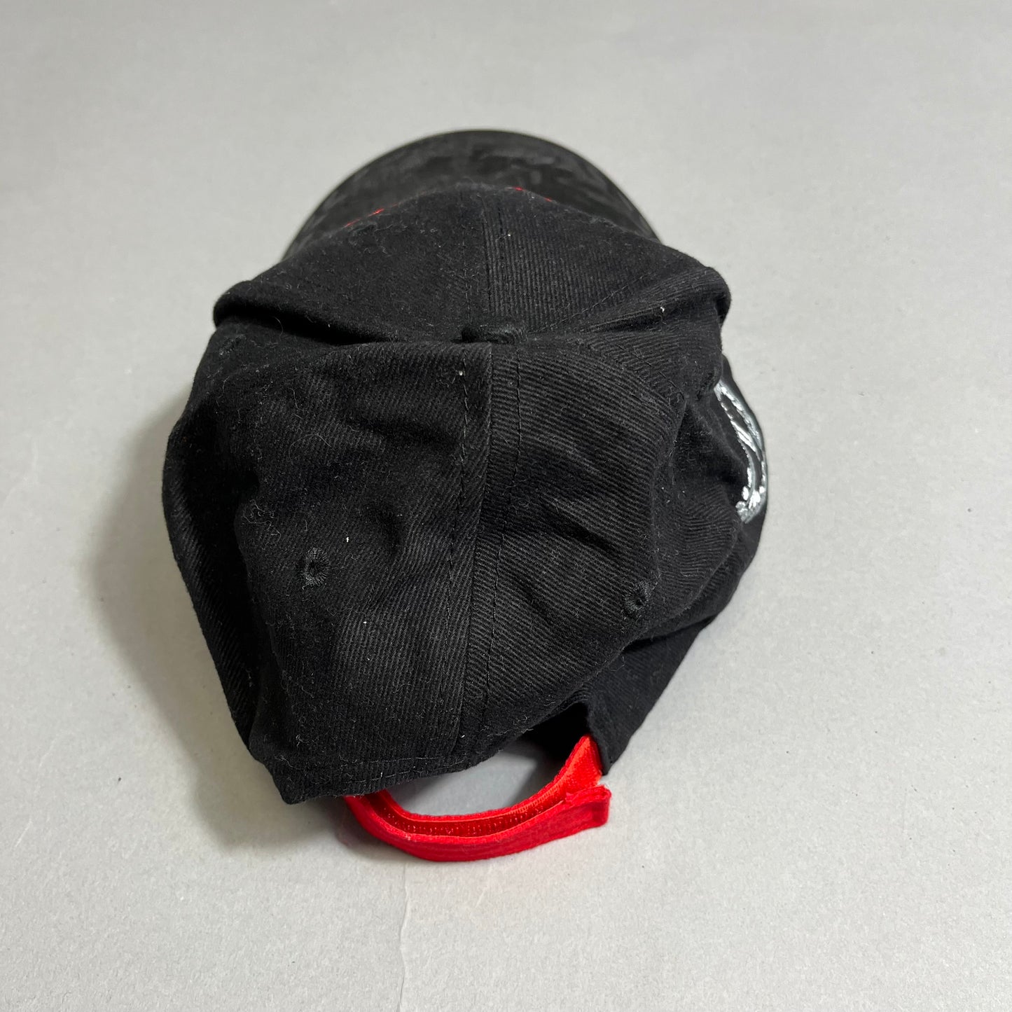 Black baseball cap with a red adjustable strap on a gray surface.