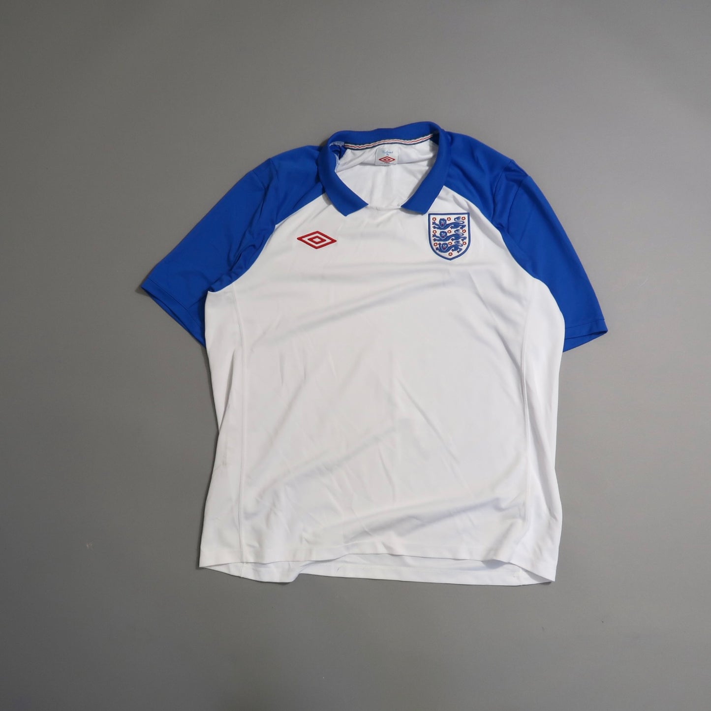 White and blue soccer jersey with England emblem on gray background.