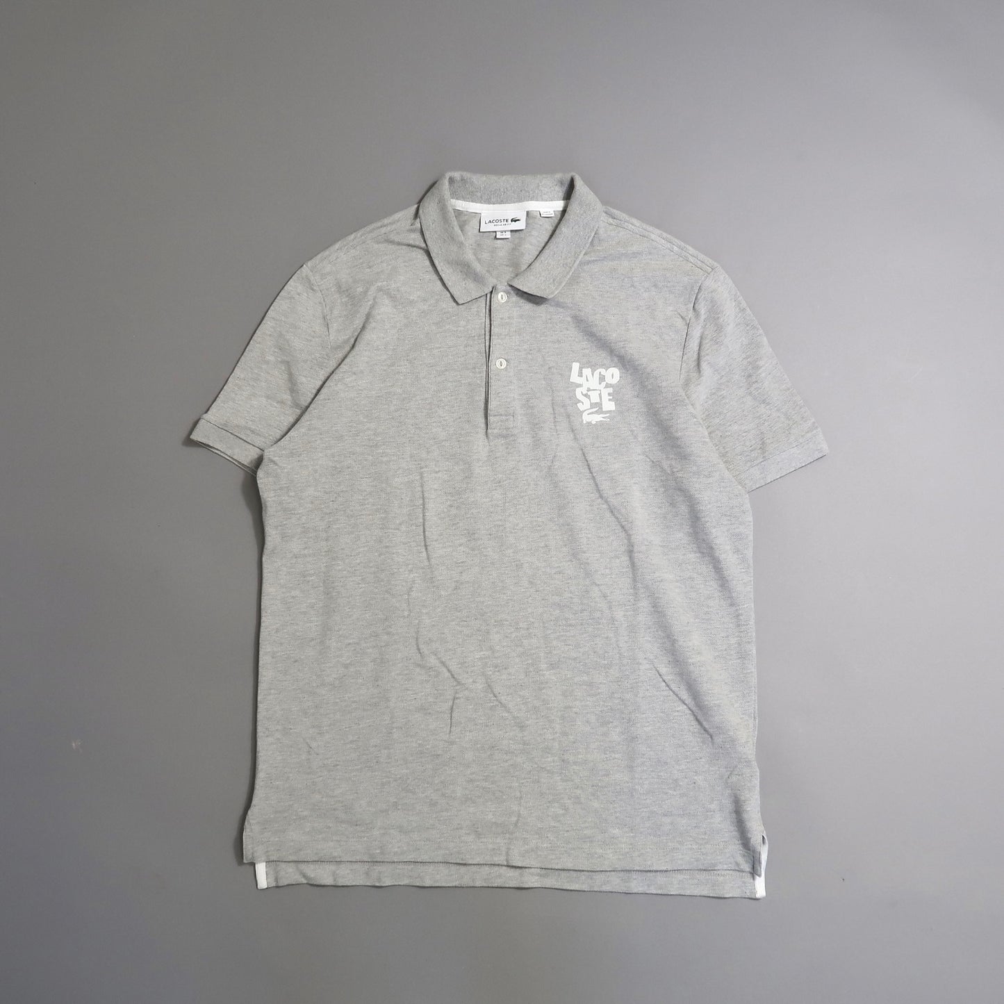 Gray polo shirt with a logo on the upper left chest on a gray background.