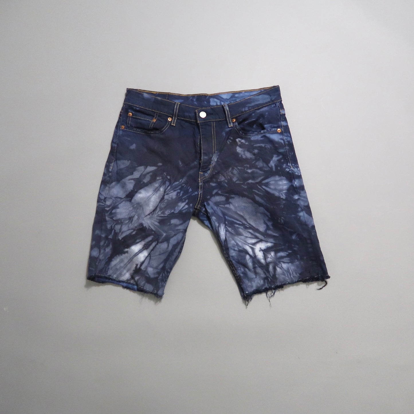 Tie-dye denim shorts with a frayed hem on a neutral background.
