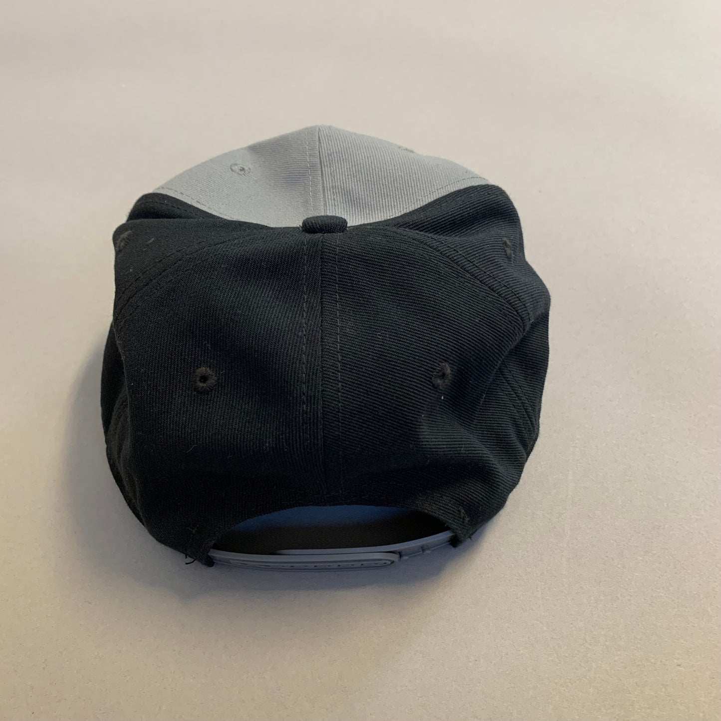 Back view of a two-tone snapback cap on a gray surface.
