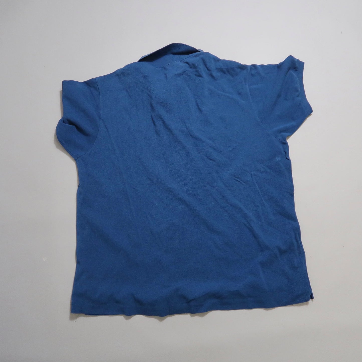 Blue T-shirt lying flat on a neutral surface, viewed from the back.