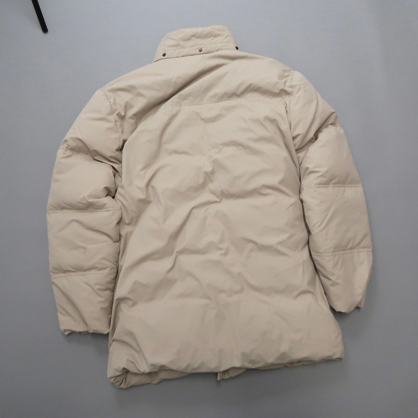 Beige puffer coat laid flat on a gray surface.