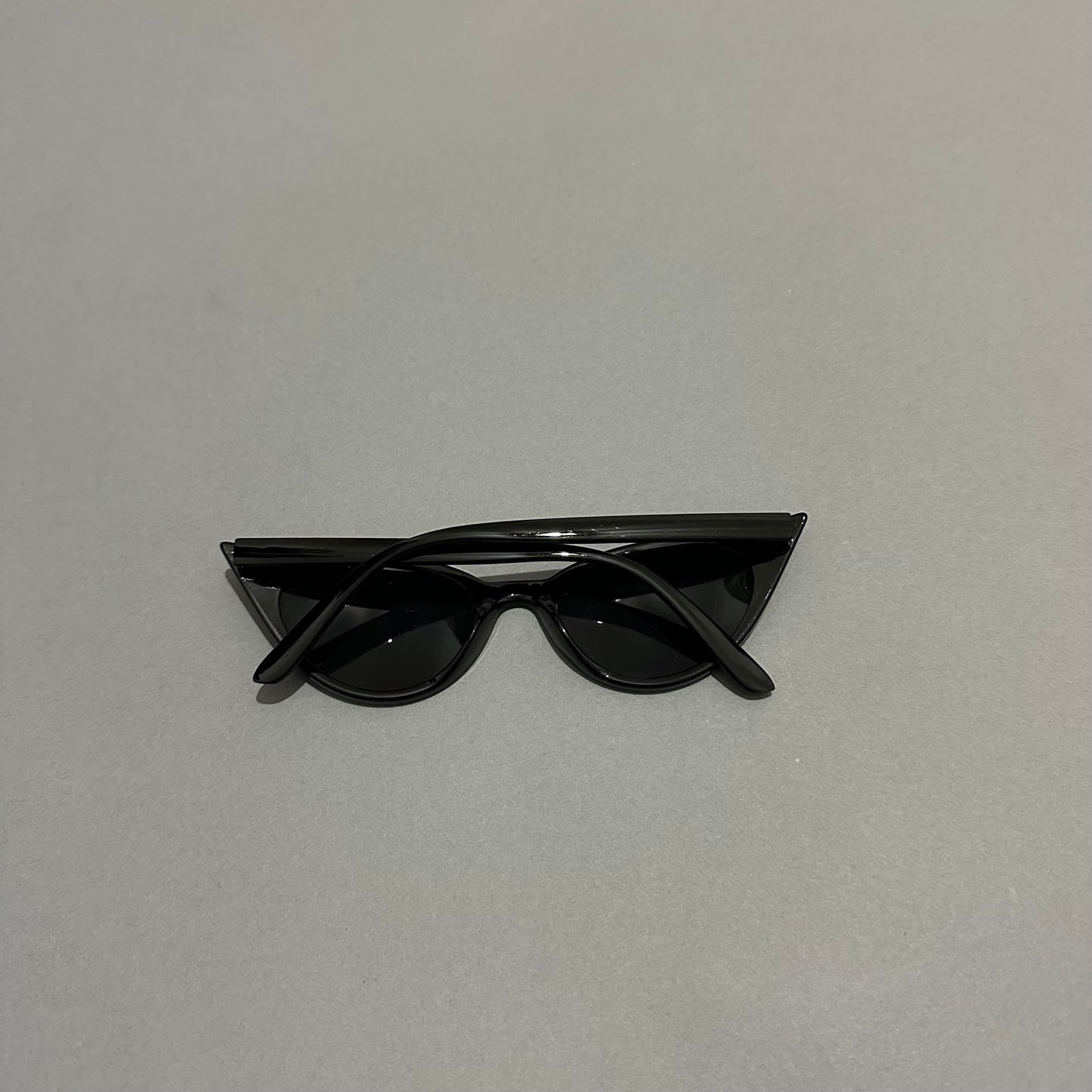 Black cat-eye sunglasses on a light gray background.