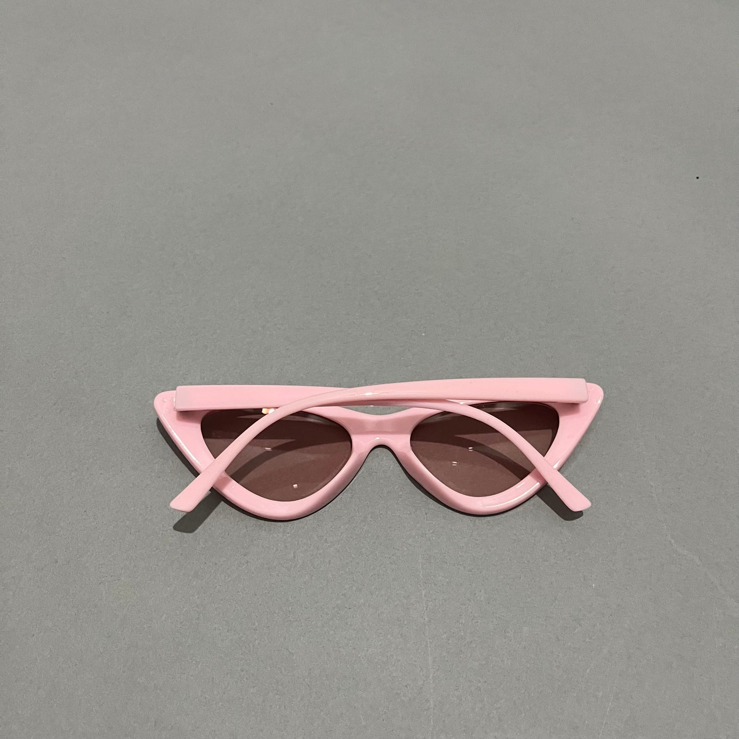 Pink cat-eye sunglasses on a gray surface.