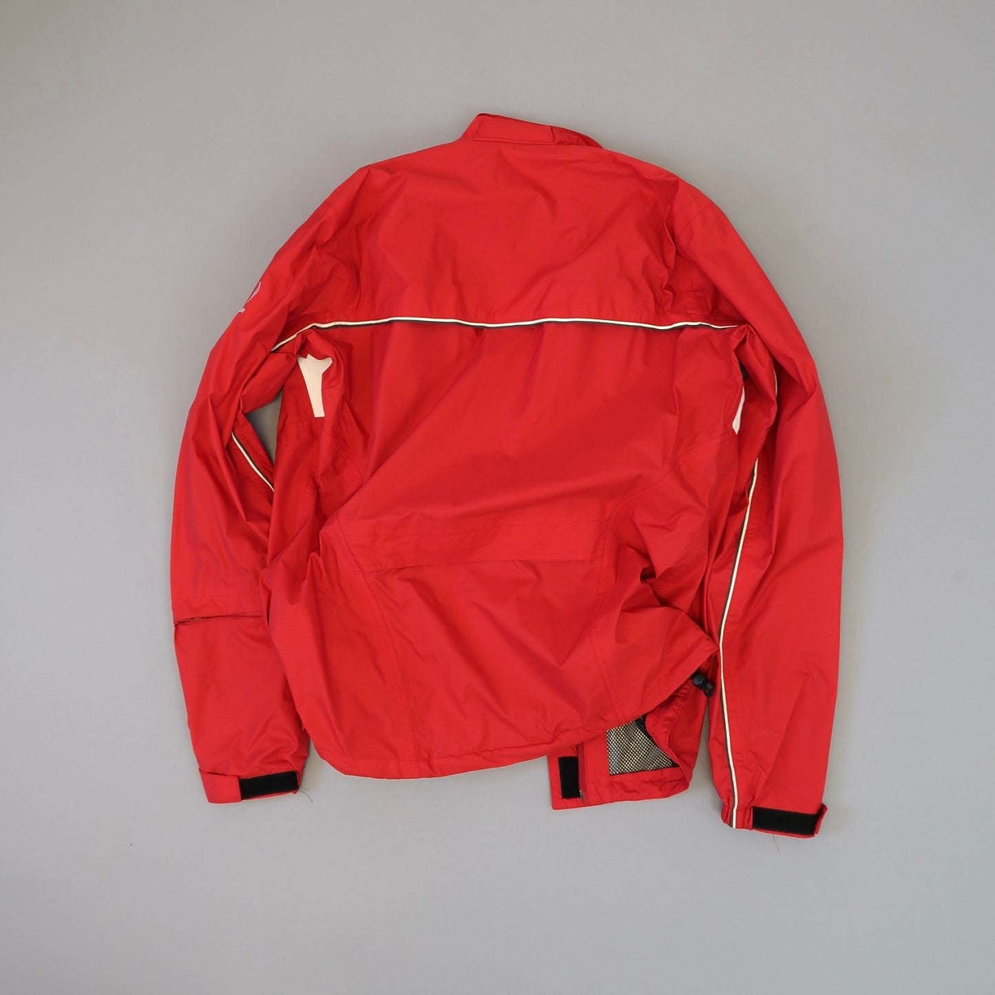 Red jacket with white piping laid flat on a gray surface.