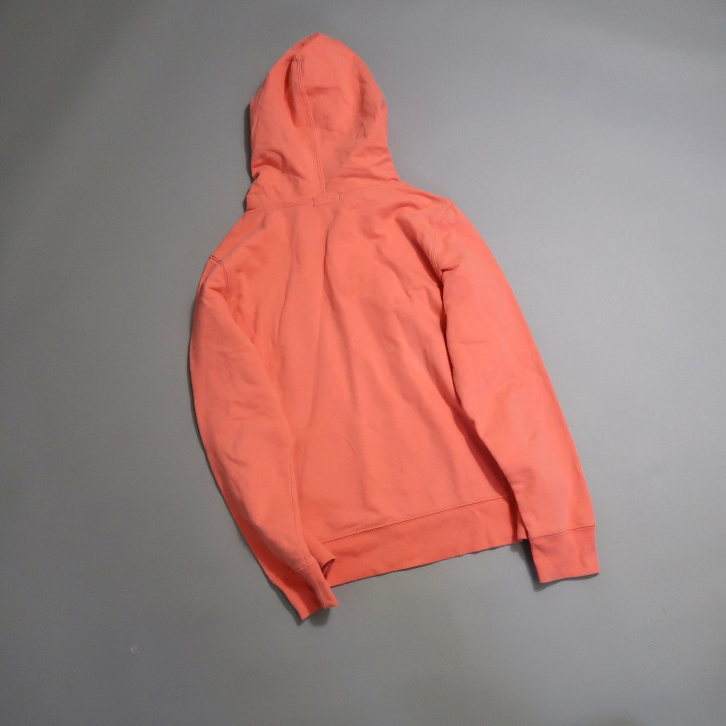 Pink hoodie on a gray surface, viewed from the back.