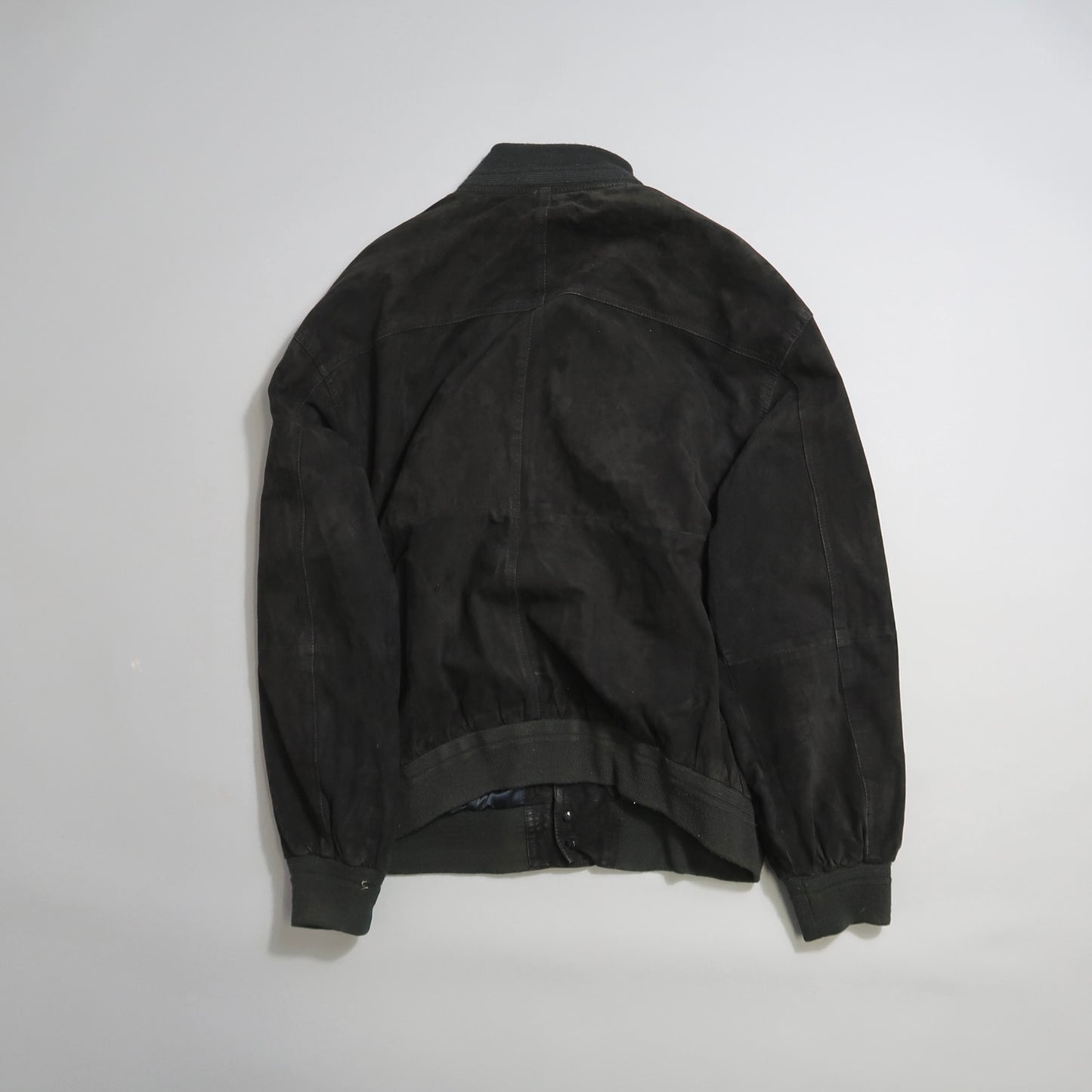 Back view of a black bomber jacket on a white background.