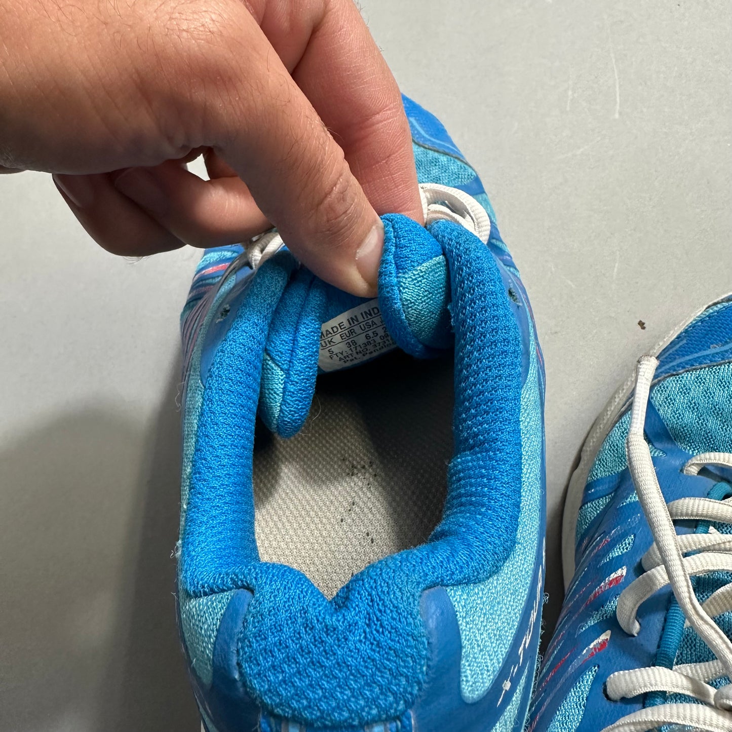 Hand holding open a blue sneaker for label visibility.