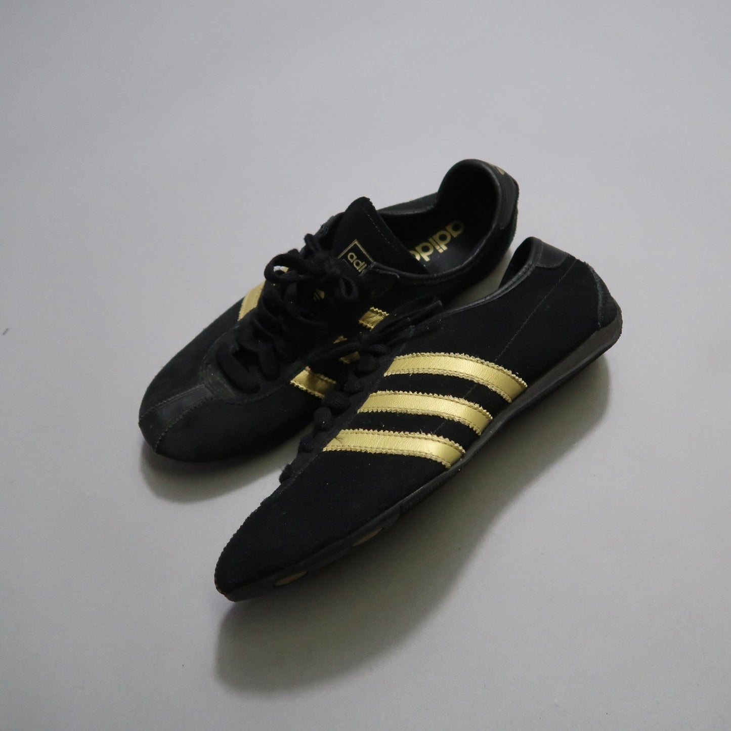 Black sneakers with gold stripes on a plain background.