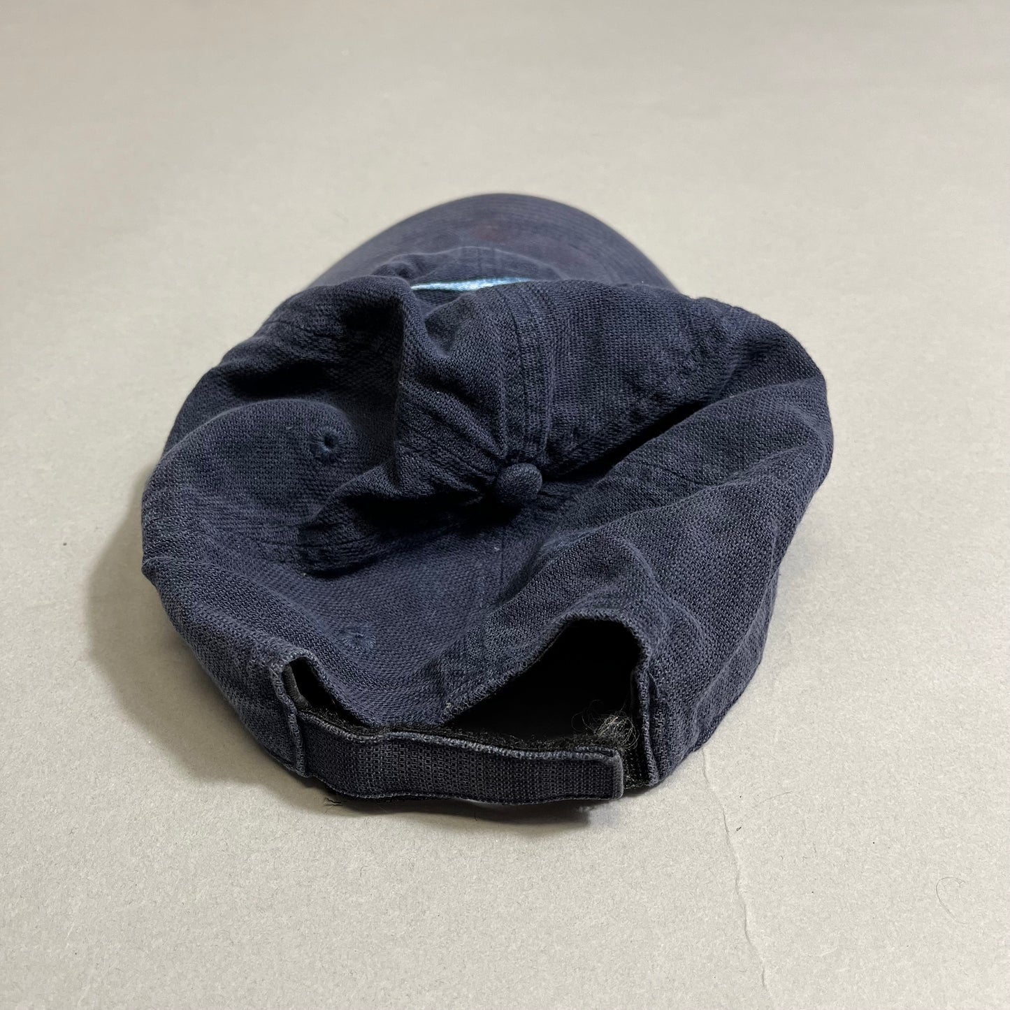 Navy blue cap lying upside down on a gray surface.