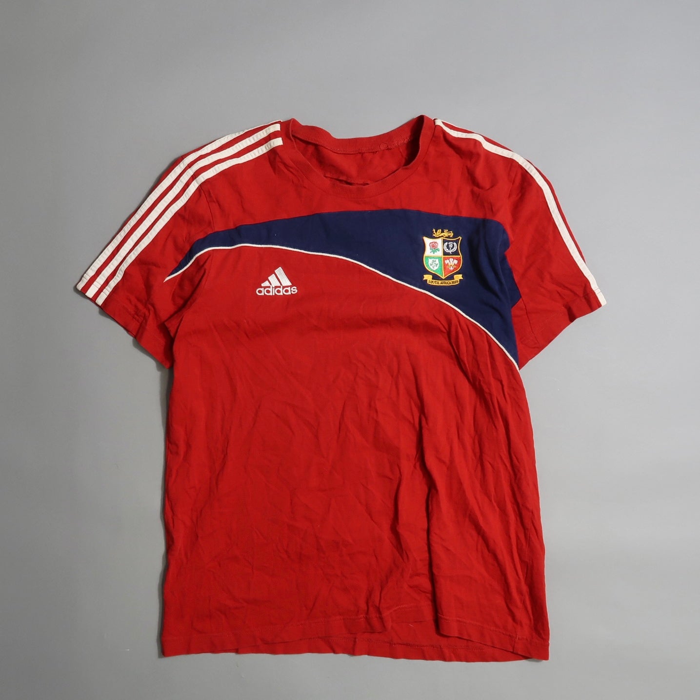 Red Adidas shirt with stripes and embroidered crest on chest.