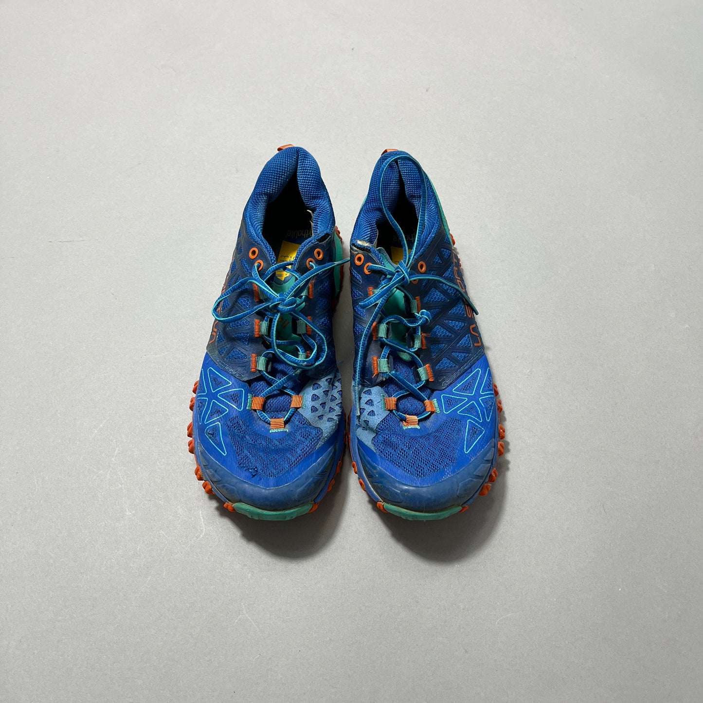 Blue and orange trail running shoes on a gray background.