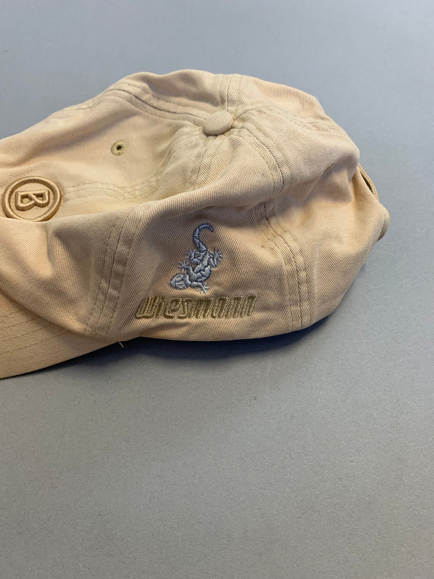 Beige cap with embroidered scorpion and text on a grey surface.