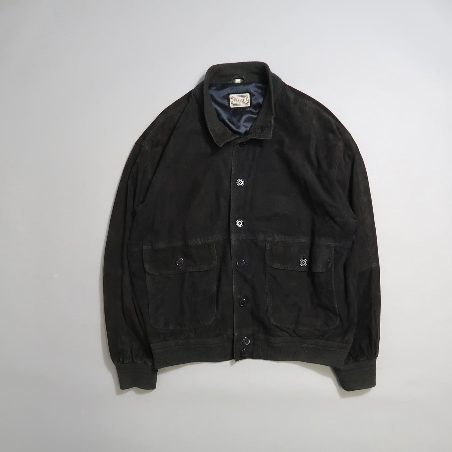 Black jacket with button front and two flap pockets on a neutral background.