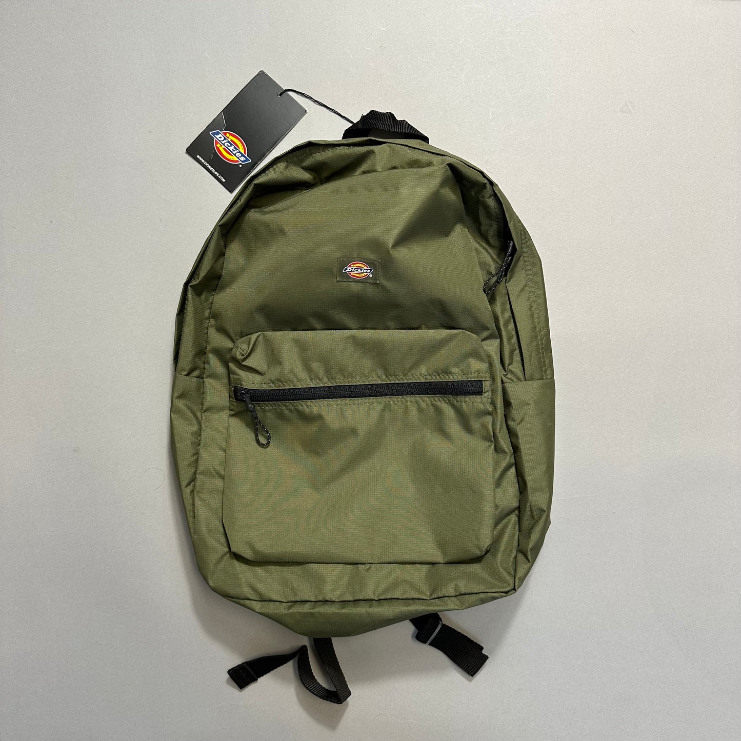Green backpack with front pocket and tag attached on a light background.
