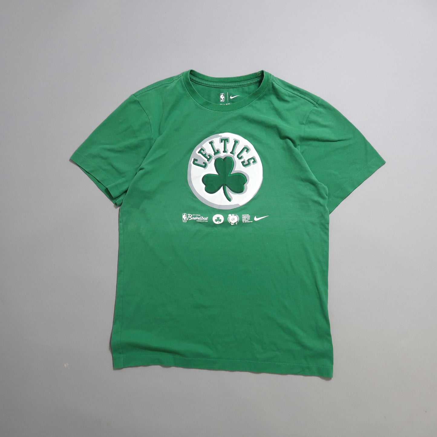 Green Celtics T-shirt with shamrock logo on a gray background.