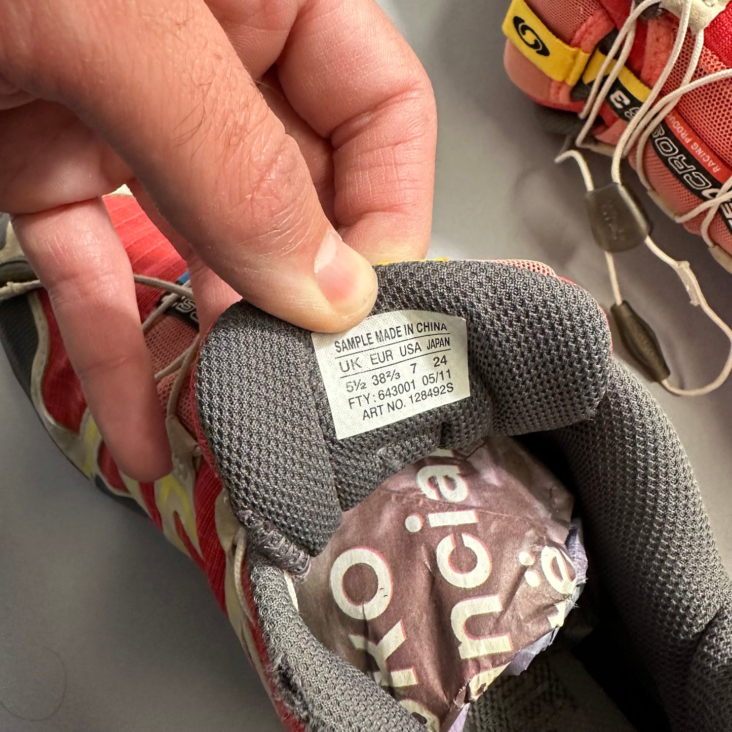 Hand holding shoe tongue label with size and origin details.