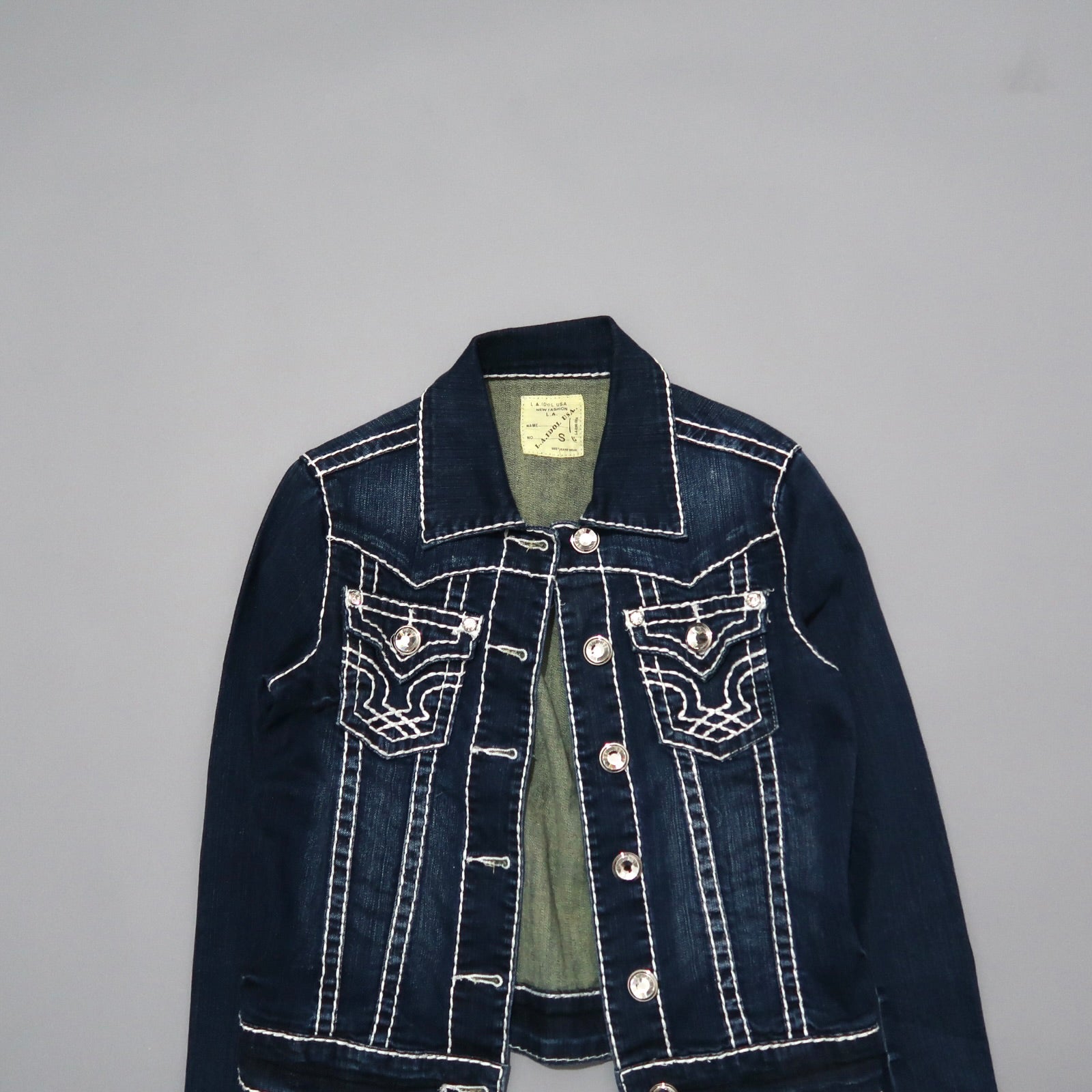 Dark denim jacket with decorative stitching, buttoned front on gray background.